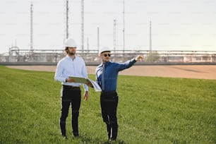 Due giovani ingegneri in piedi all'aperto vicino alla raffineria di petrolio, discutendo di problemi. Copia spazio.