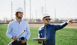 Two young engineers with hard hat standing outdoors by oil refinery, discussing issues. Copy space.