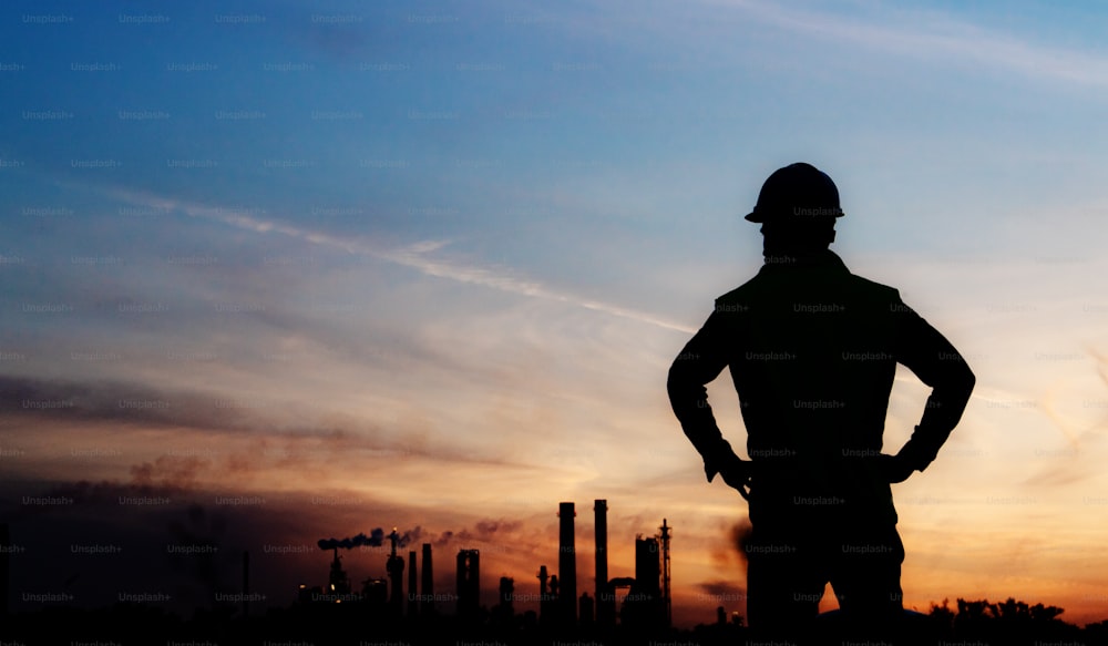 Young engineer with hard hat and tablet standing outdoors by oil refinery. Copy space.