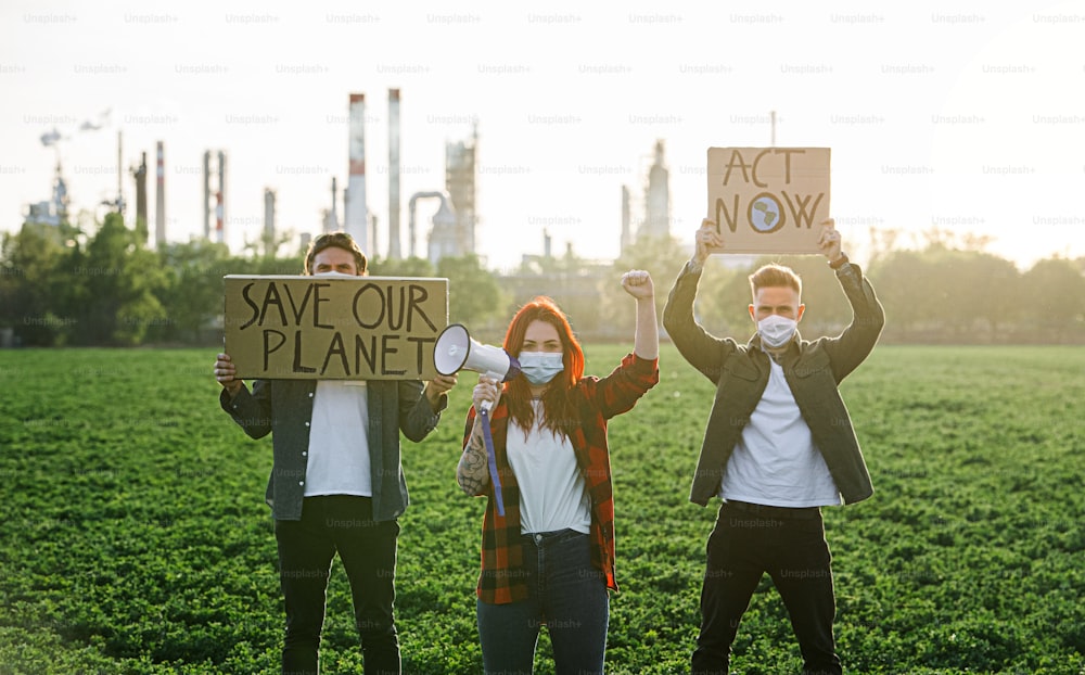 プラカードとメガホンを持った若い活動家のグループが石油精製所のそばに立って抗議している。