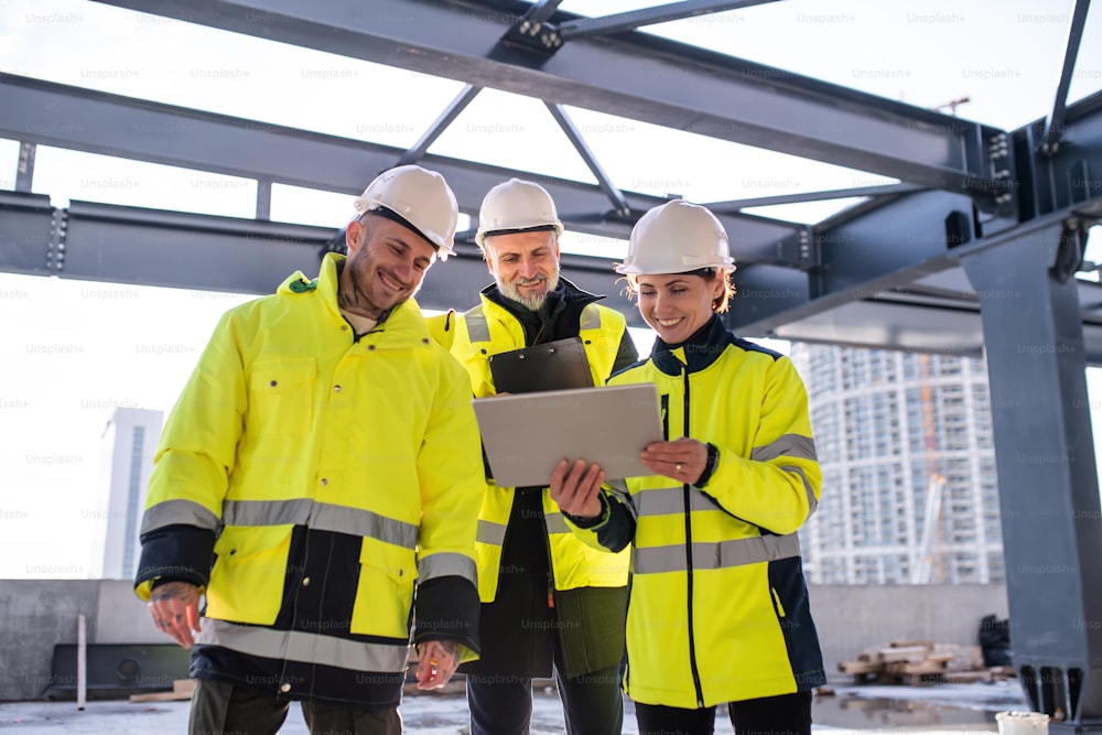 A group of engineers standing outdoors on construction site, using tablet.