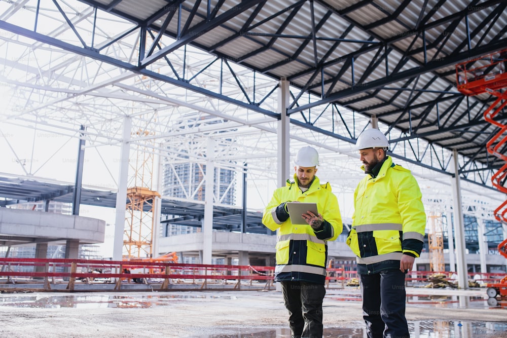 Men engineers standing outdoors on construction site, using tablet. Copy space.