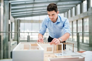 Young businessman or architect with model of a house standing at the desk in office, working.