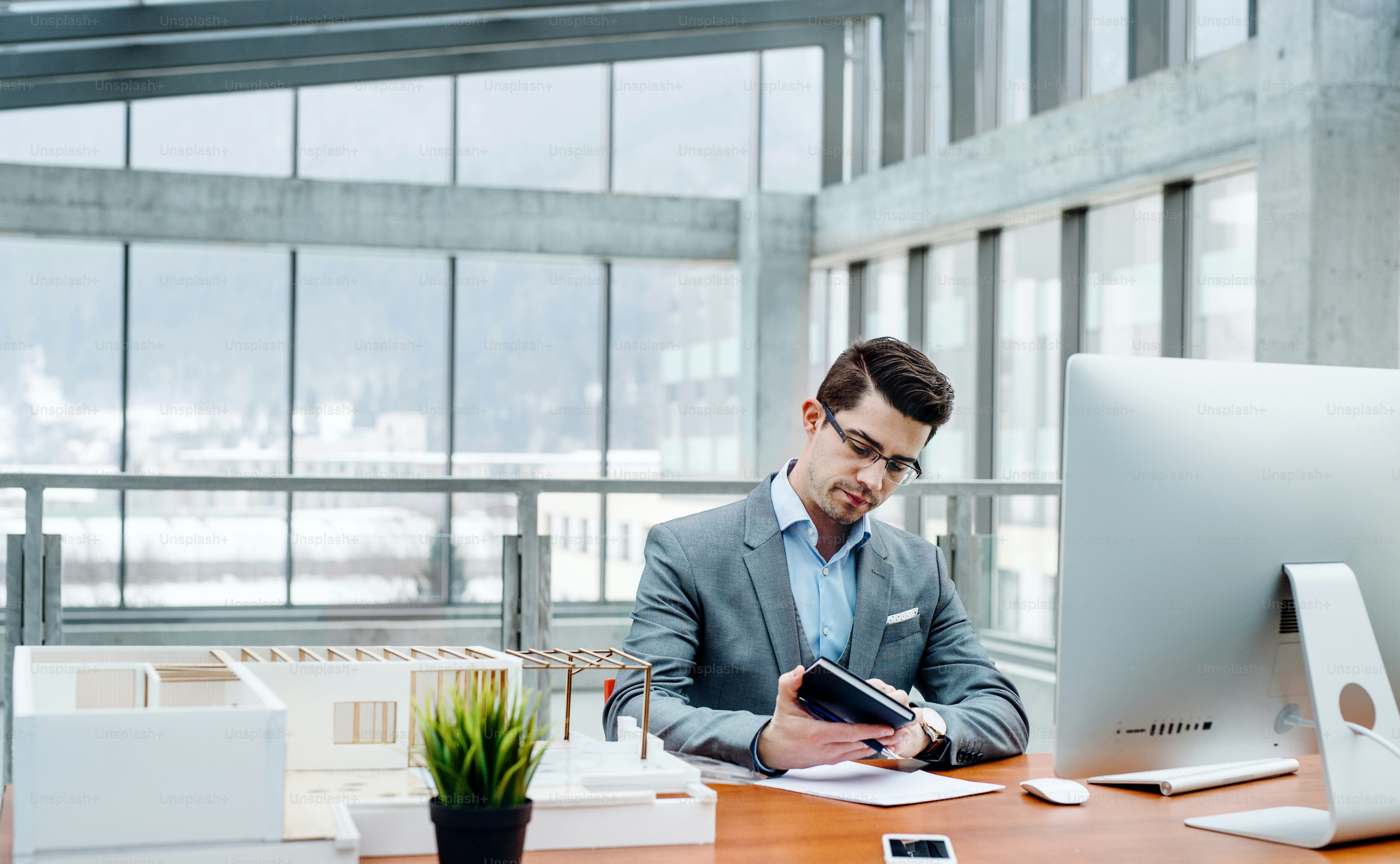 Young businessman or architect with model of a house sitting at the desk in office, working.
