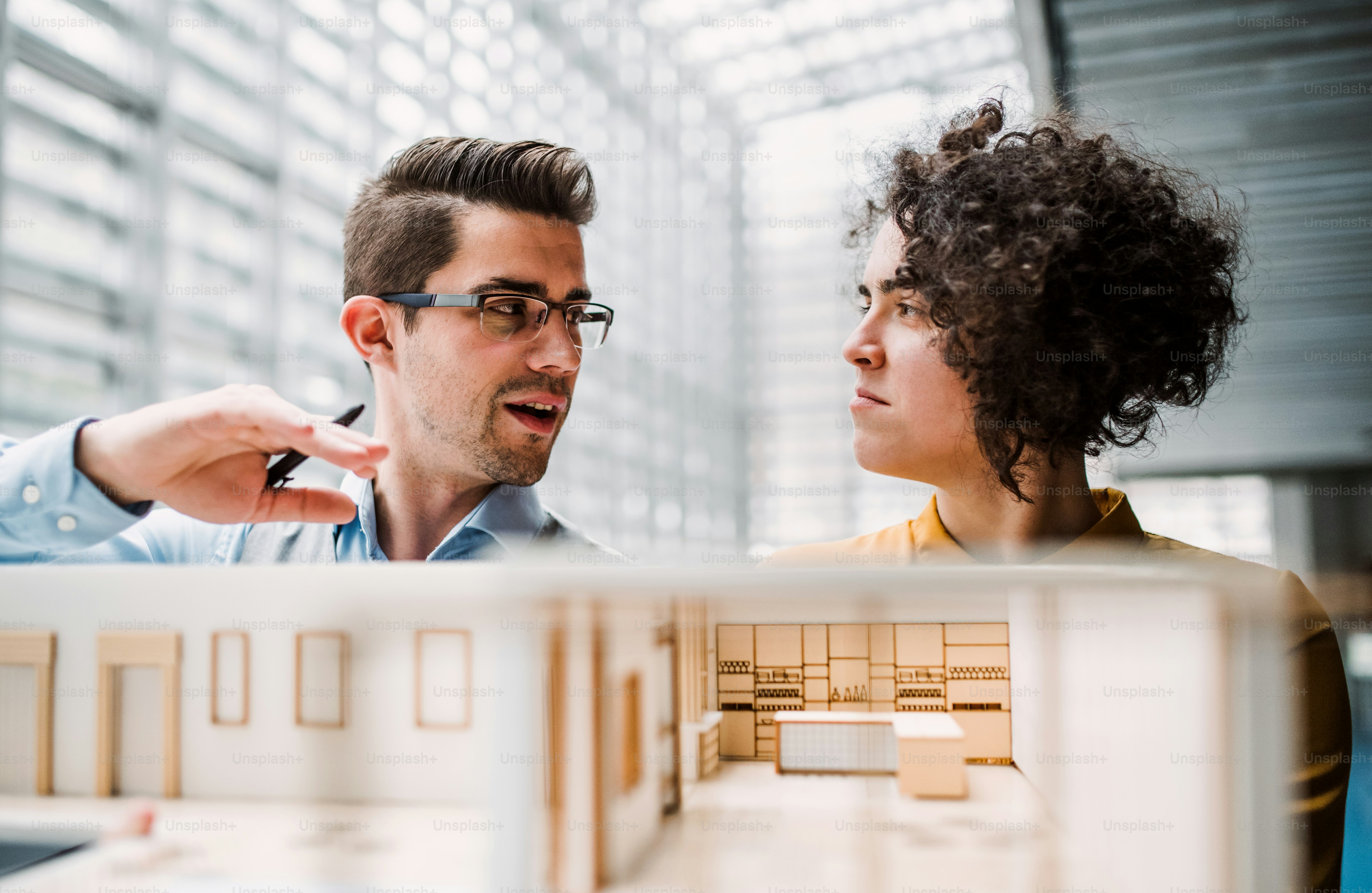 Two young architects with model of a house standing in office, working and talking.