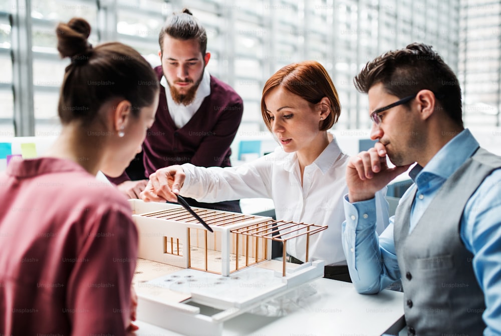 Eine Gruppe junger Architekten mit dem Modell eines Hauses, die im Büro arbeiten und sich unterhalten.