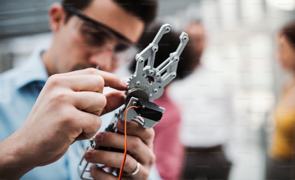 Um jovem empresário ou cientista com mão robótica e óculos de segurança em pé no escritório, trabalhando.