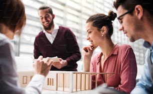 A group of young architects with model of a house standing in office, working and talking.