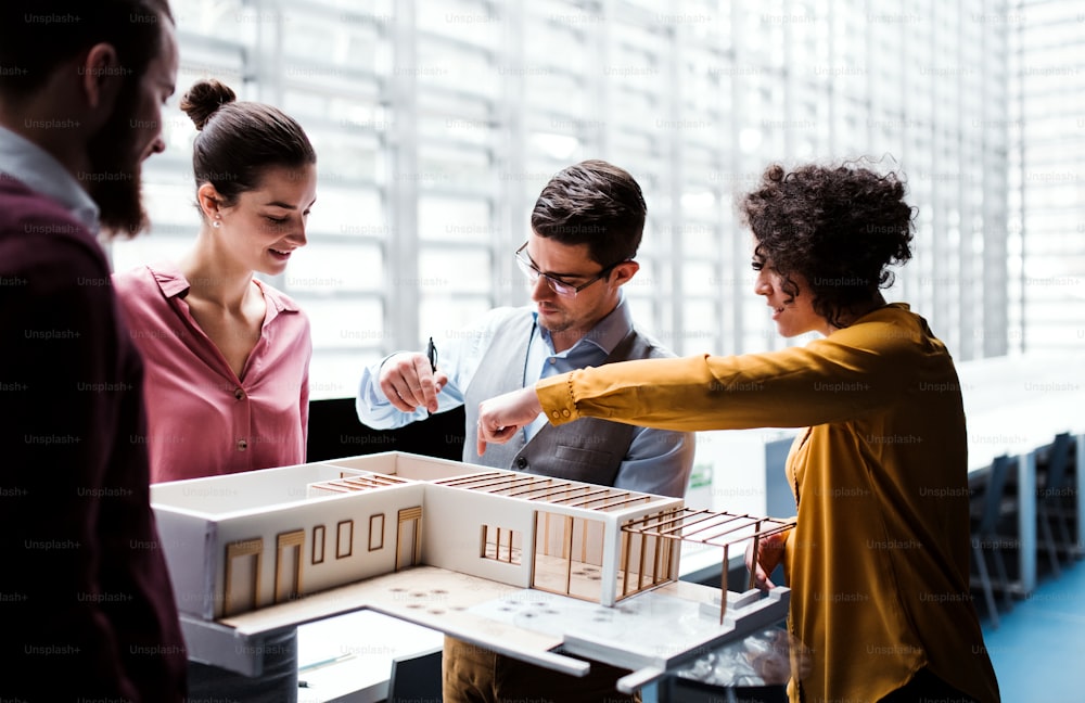 Eine Gruppe junger Architekten mit dem Modell eines Hauses, die im Büro stehen, arbeiten und reden.
