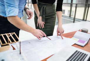 Au milieu d’une section de jeunes architectes avec des plans et une maquette d’une maison debout dans un bureau, parlant.