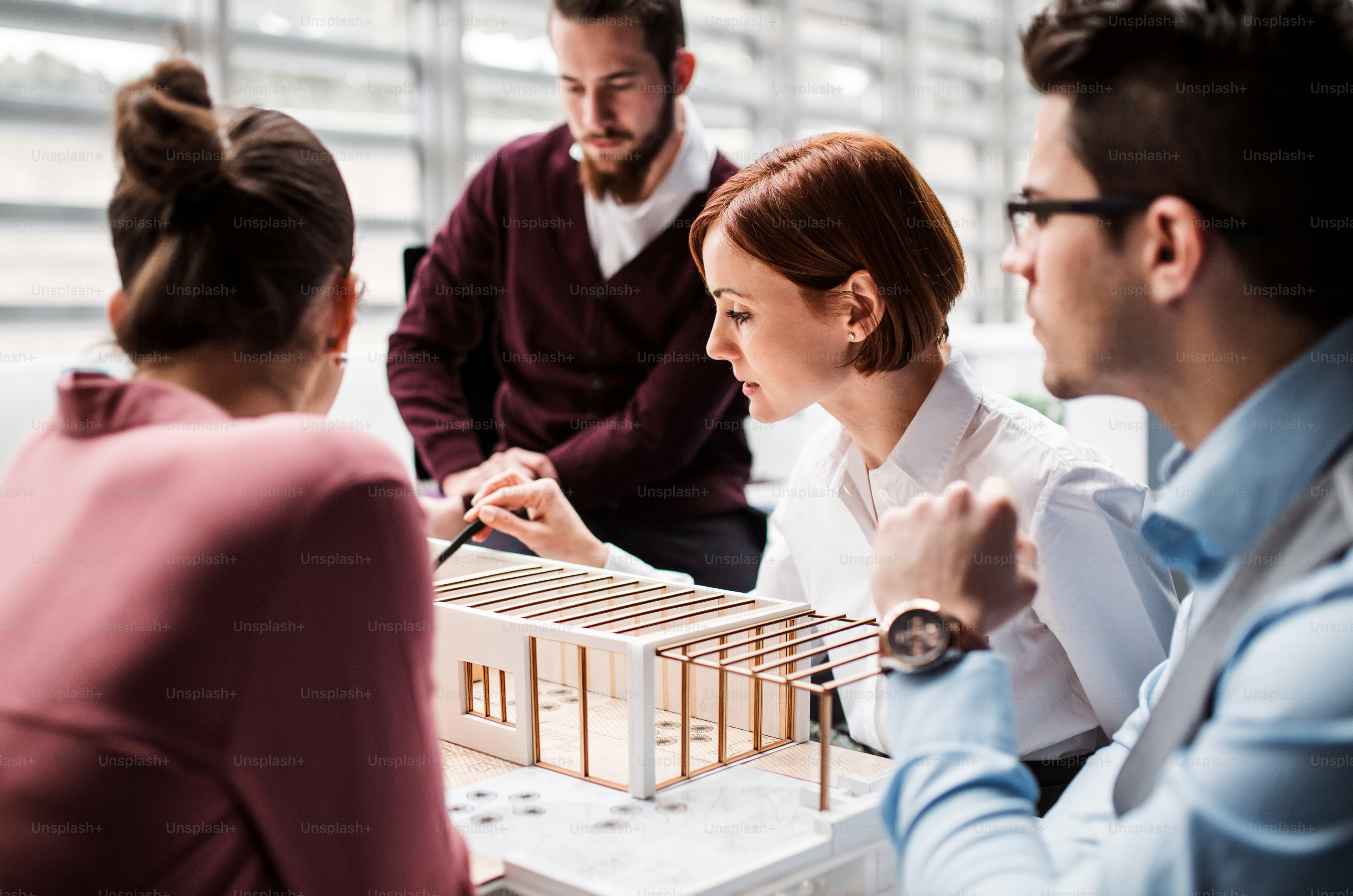 A group of young architects with model of a house standing in office, working and talking.