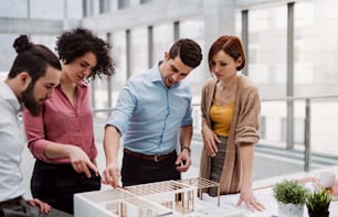 A group of young architects with model of a house standing in office, working and talking.
