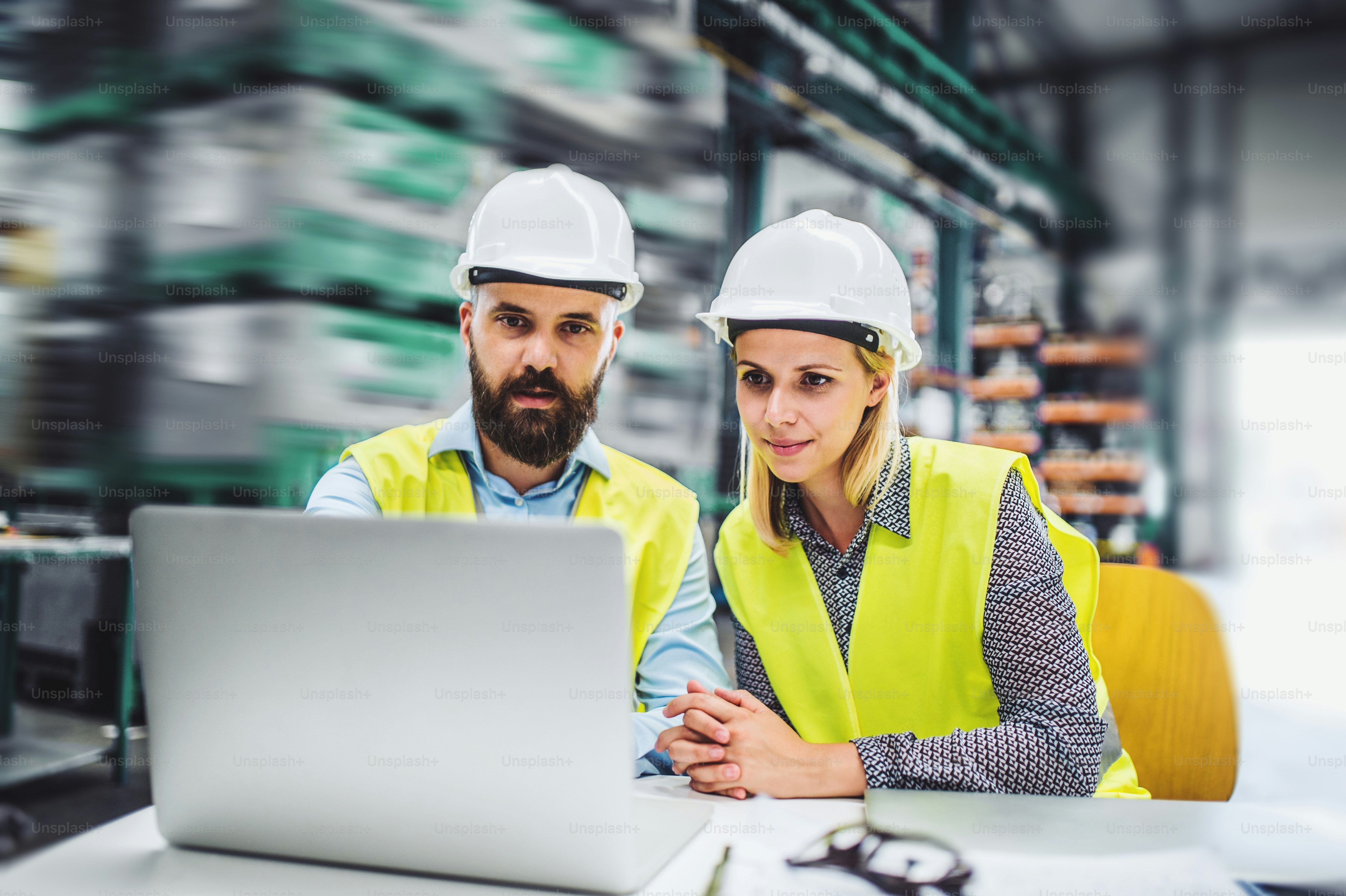 A portrait of a mature industrial man and woman engineer with laptop in a factory, working.