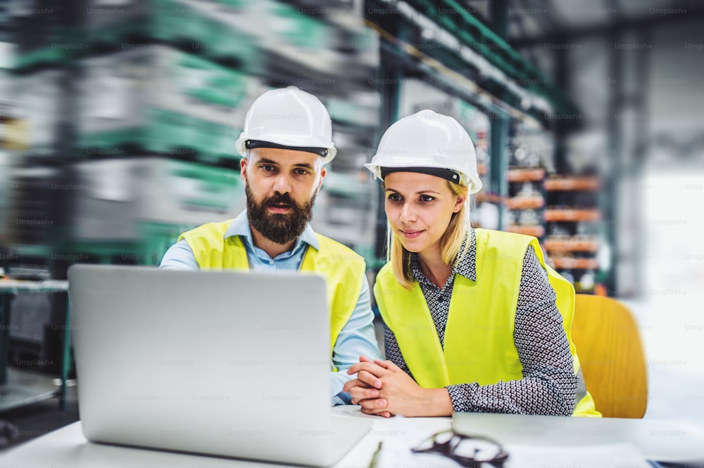 A portrait of a mature industrial man and woman engineer with laptop in a factory, working.