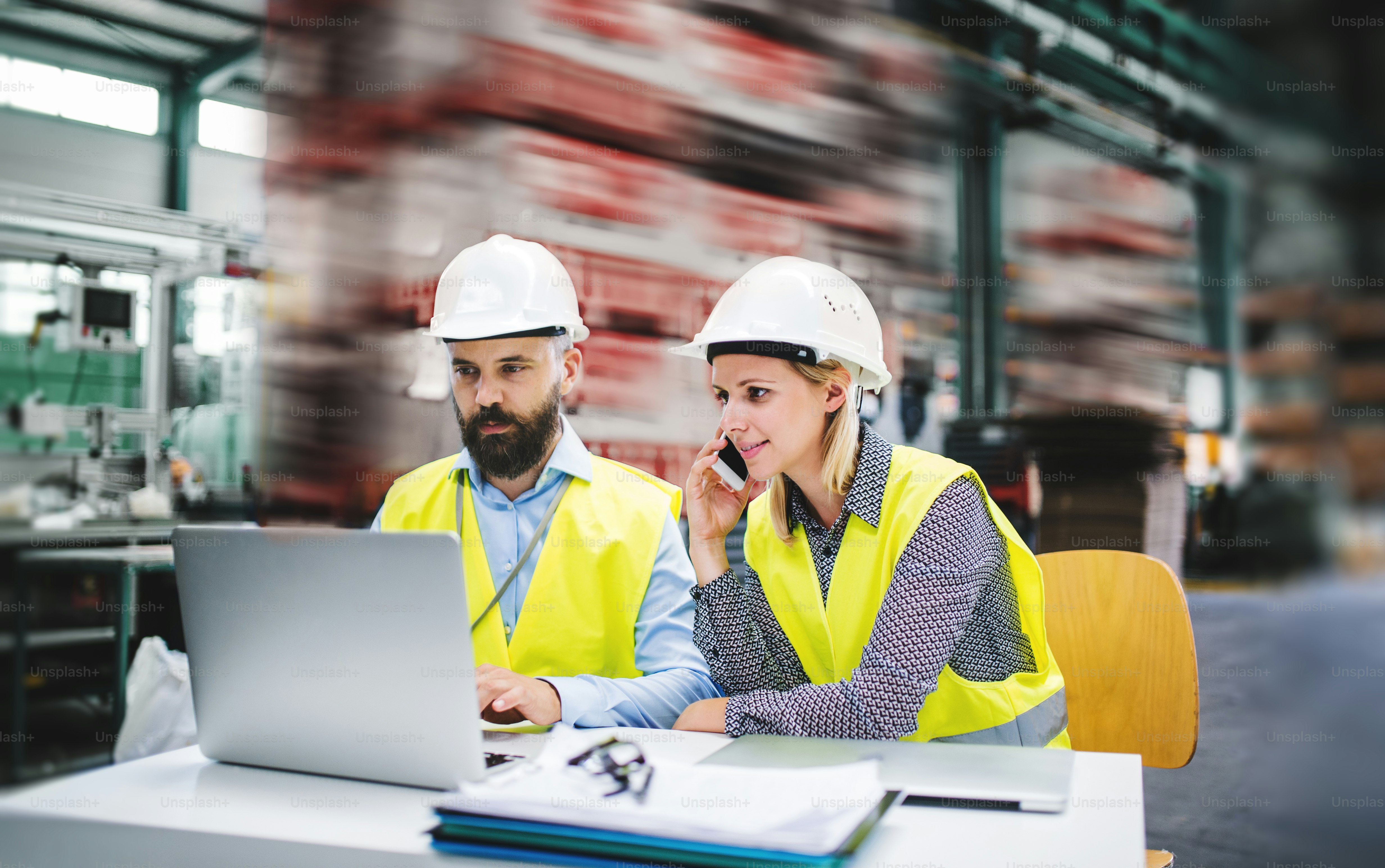 A portrait of a mature industrial man and woman engineer with laptop and smartphone in a factory, working.