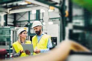A portrait of a mature industrial man and woman engineer with tablet in a factory. Copy space.
