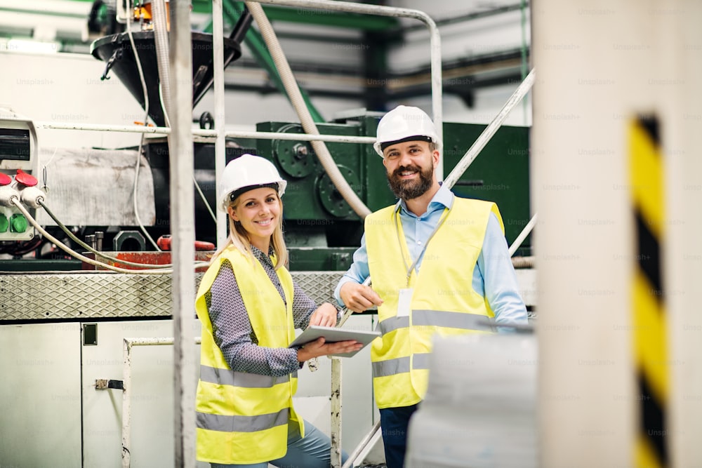 A portrait of a mature industrial man and woman engineer with tablet in a factory.