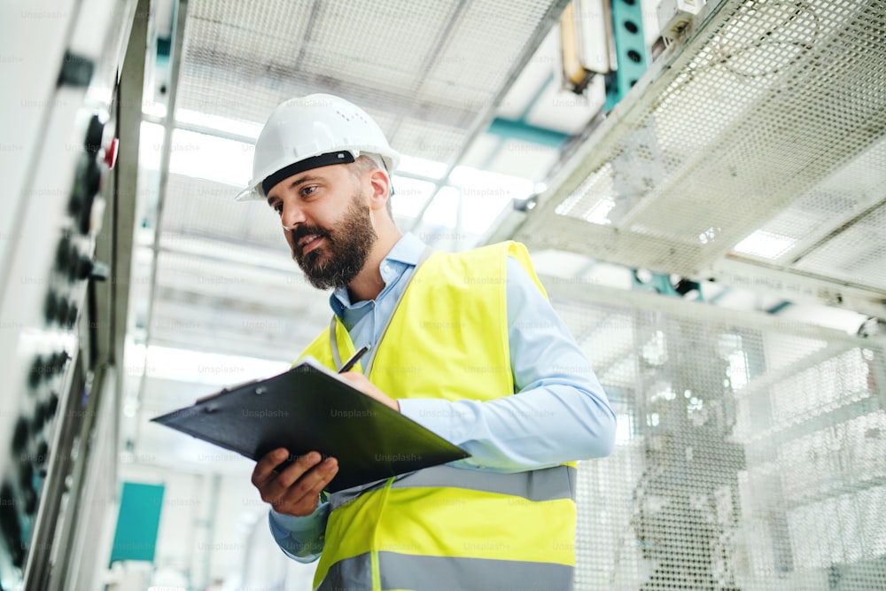 A portrait of a mature industrial man engineer with clipboard in a factory, working. Copy space.