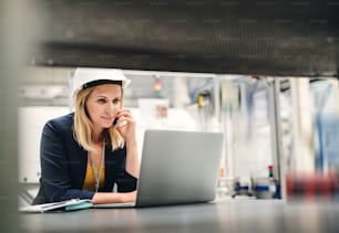 An industrial woman engineer in a factory using laptop and smartphone.