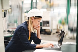 Una vista laterale di una donna ingegnere industriale in una fabbrica che utilizza laptop e smartphone.