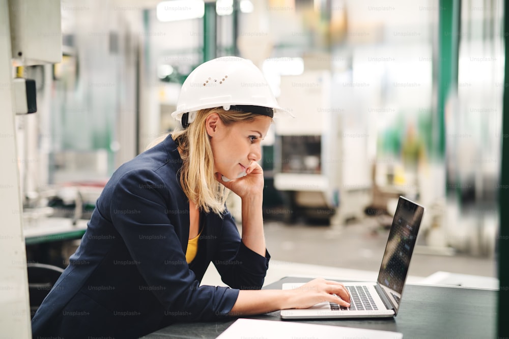 A side view of industrial woman engineer in a factory using laptop and smartphone.