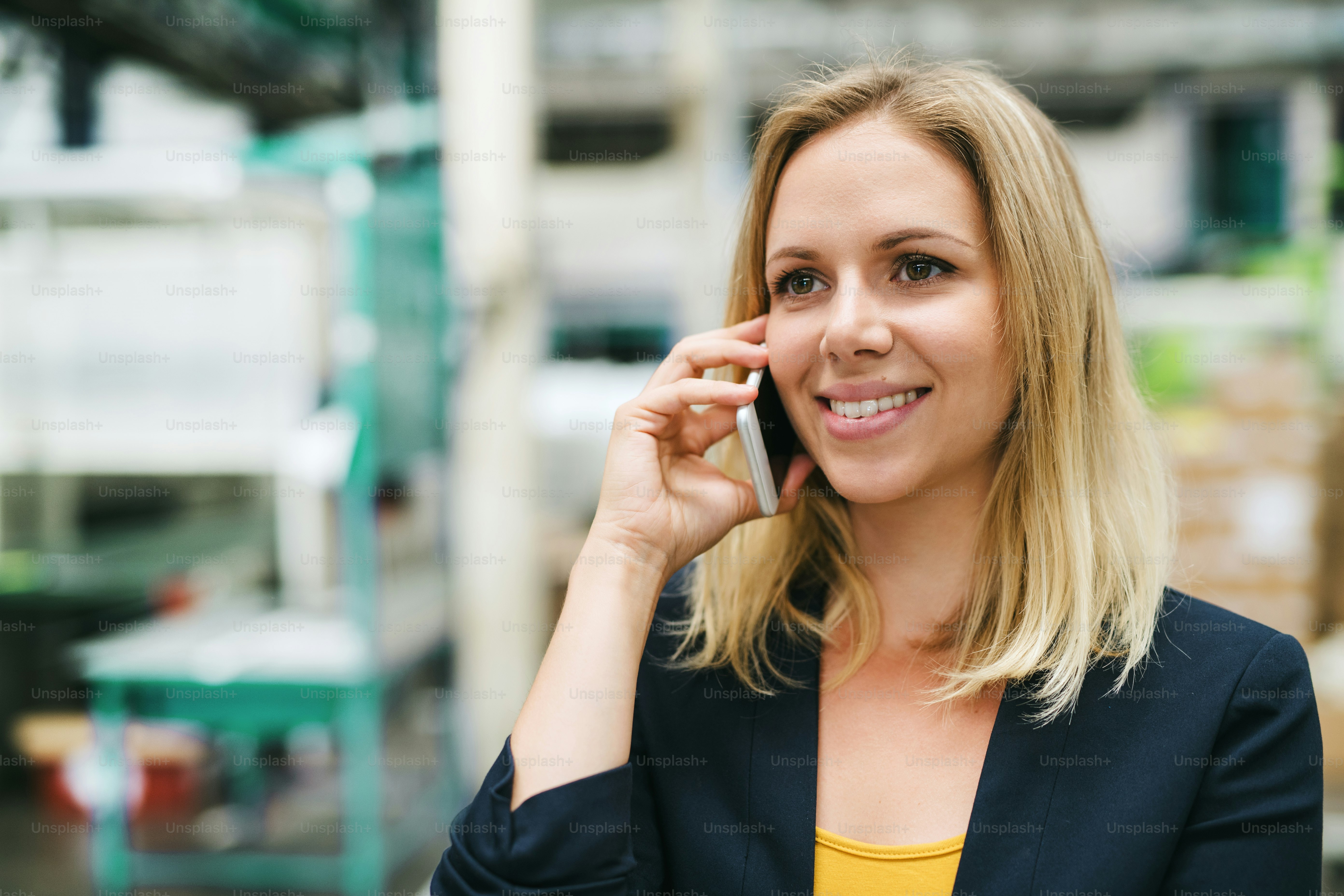 Ein Porträt einer glücklichen Industrieingenieurin am Telefon, die in einer Fabrik steht.