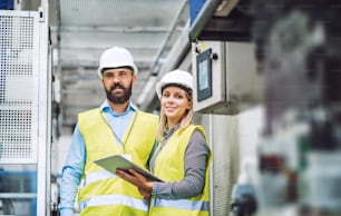 A portrait of a mature industrial man and woman engineer with tablet in a factory. Copy space.