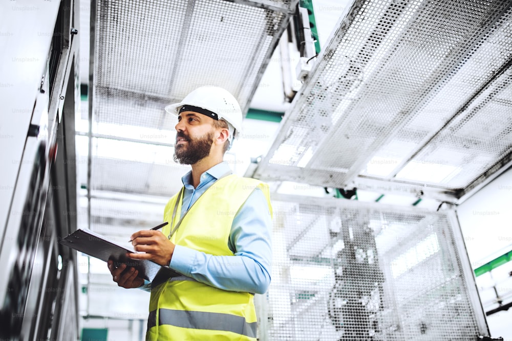 Portrait d’un ingénieur industriel mûr avec presse-papiers dans une usine, en train de travailler. Espace de copie.