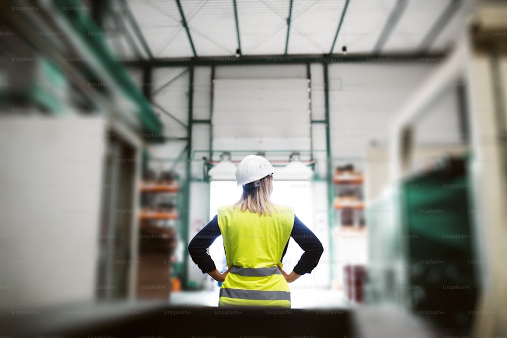 A rear view of an industrial woman engineer standing in a factory, arms on hips. Copy space.