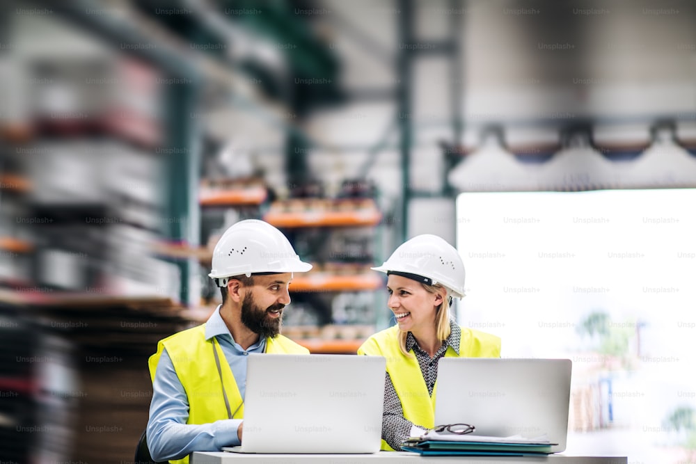 Portrait d’un industriel mûr et d’une ingénieure avec un ordinateur portable dans une usine, en train de travailler.