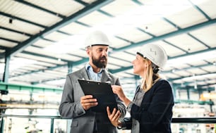 Ein Porträt eines ernsthaften, reifen Industrieingenieurs mit Klemmbrett in einer Fabrik im Gespräch.