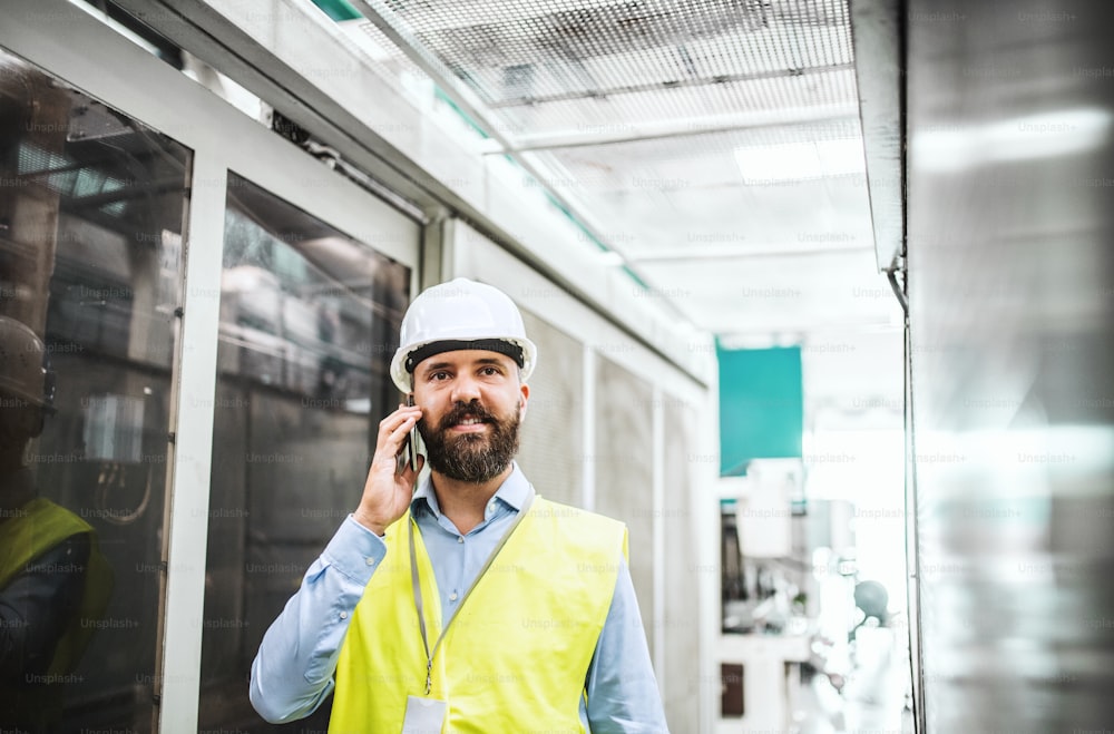 Un retrato de un ingeniero industrial maduro con un teléfono inteligente en una fábrica, haciendo una llamada telefónica.