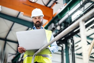 Ein Porträt eines reifen Industrieingenieurs mit Laptop in einer Fabrik, der arbeitet.