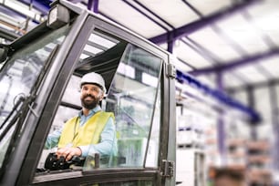 Mature industrial man engineer or driver sitting in a forklift in a factory.