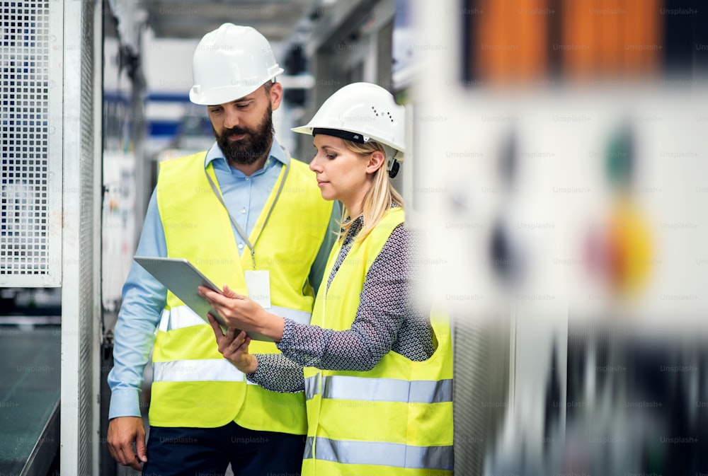 Portrait d’un industriel mûr et d’une ingénieure avec tablette dans une usine, en train de parler.