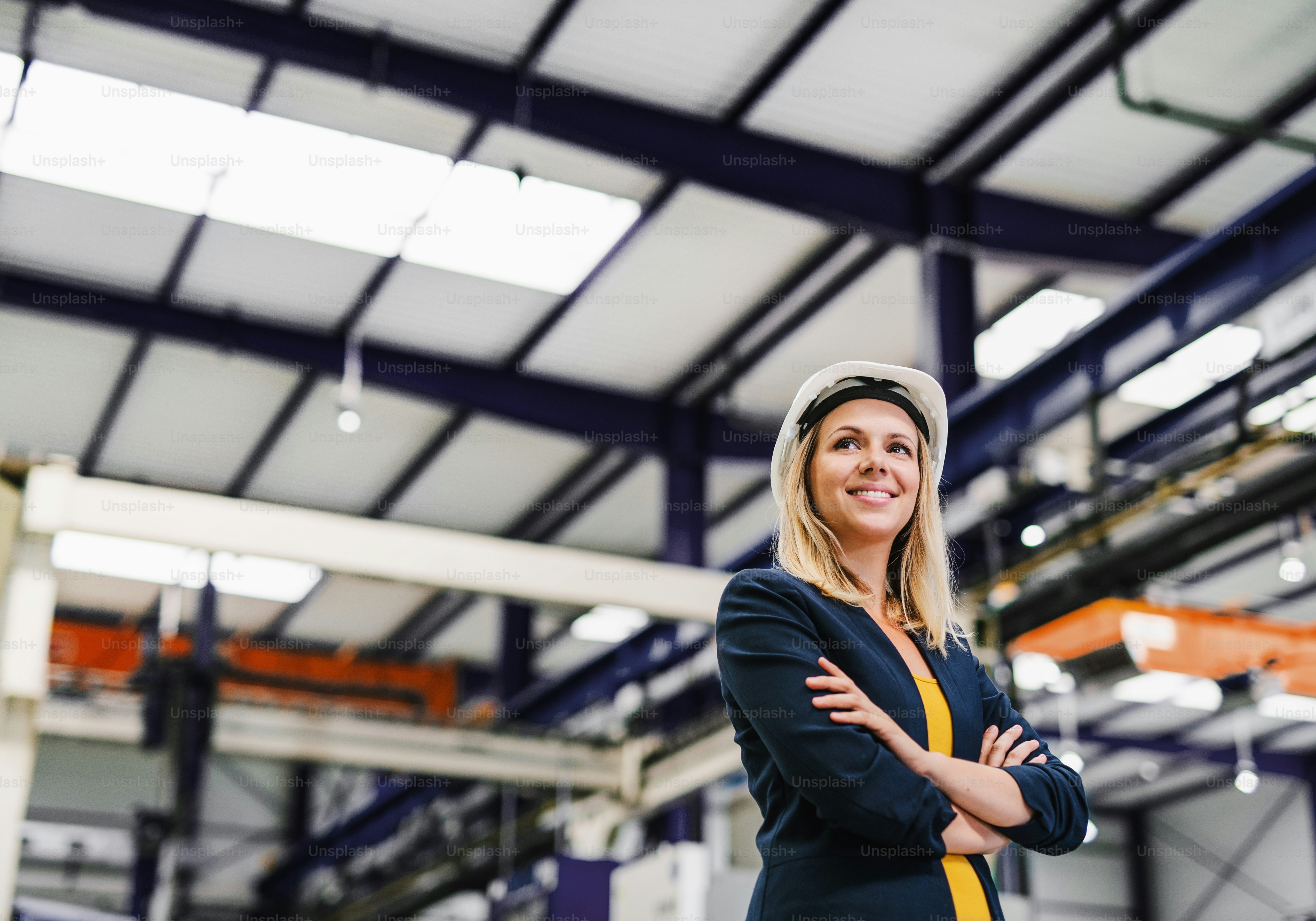 A portrait of a young industrial woman engineer standing in a factory, arms crossed. Copy space.