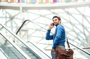 A young handsome businessman going up escalator, talking on the phone. Copy space.