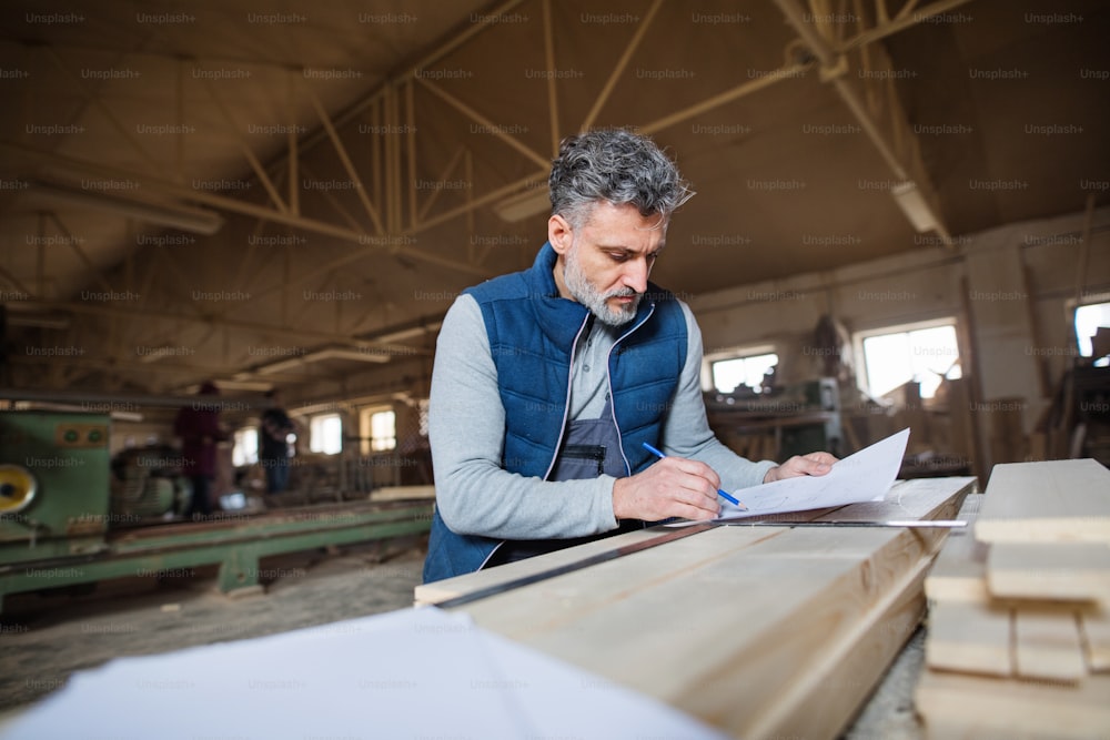 A mature man worker in the carpentry workshop, making plans.