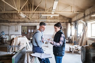 Portrait d’un homme et d’une femme ouvriers dans l’atelier de menuiserie, faisant des plans.