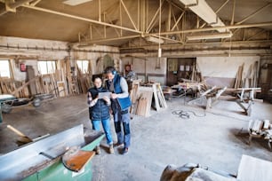 Portrait of a man and woman workers in the carpentry workshop, looking at tablet. Top view.