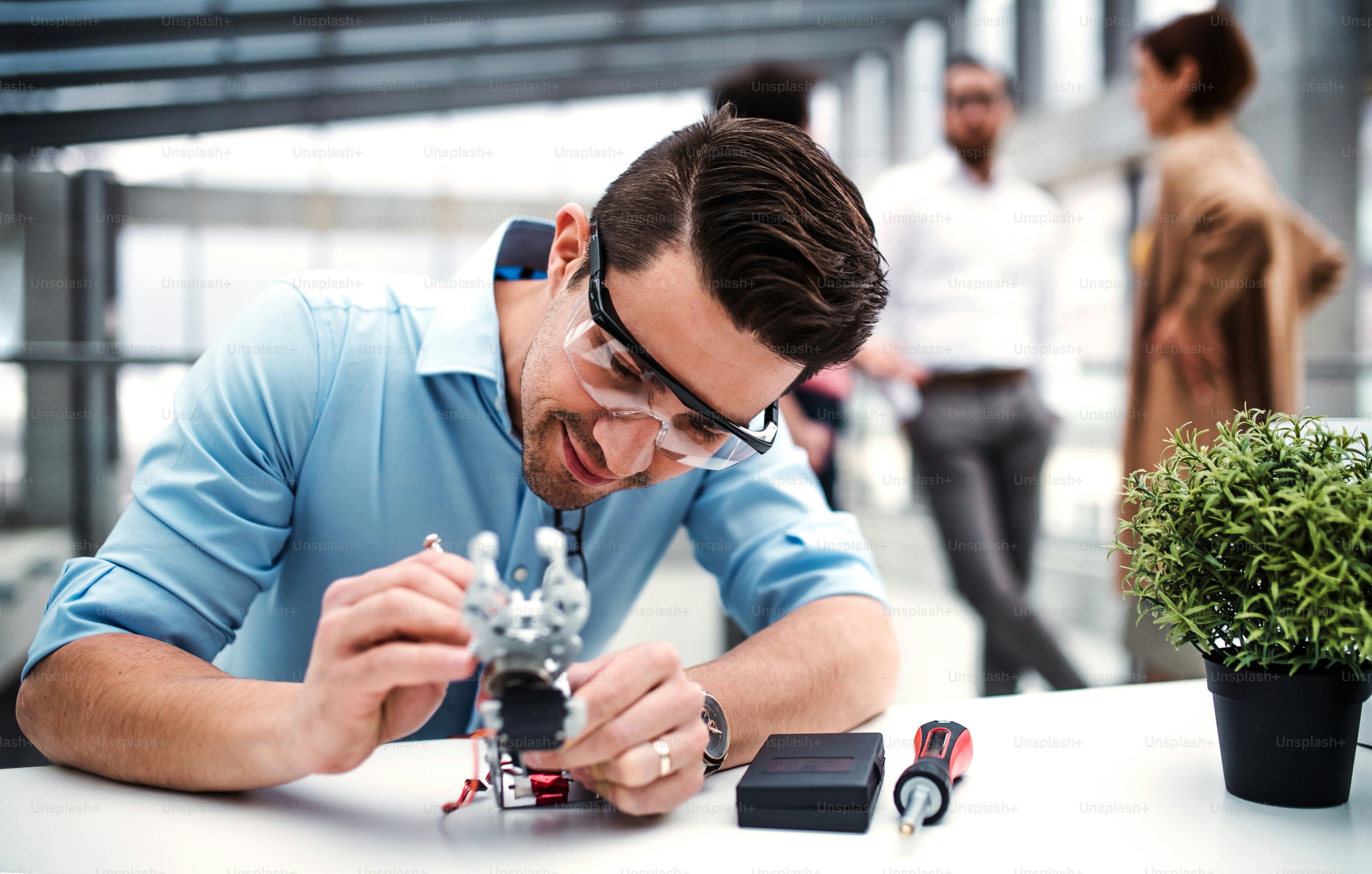 A young businessman or scientist with robotic hand and safety glasses standing in office, working