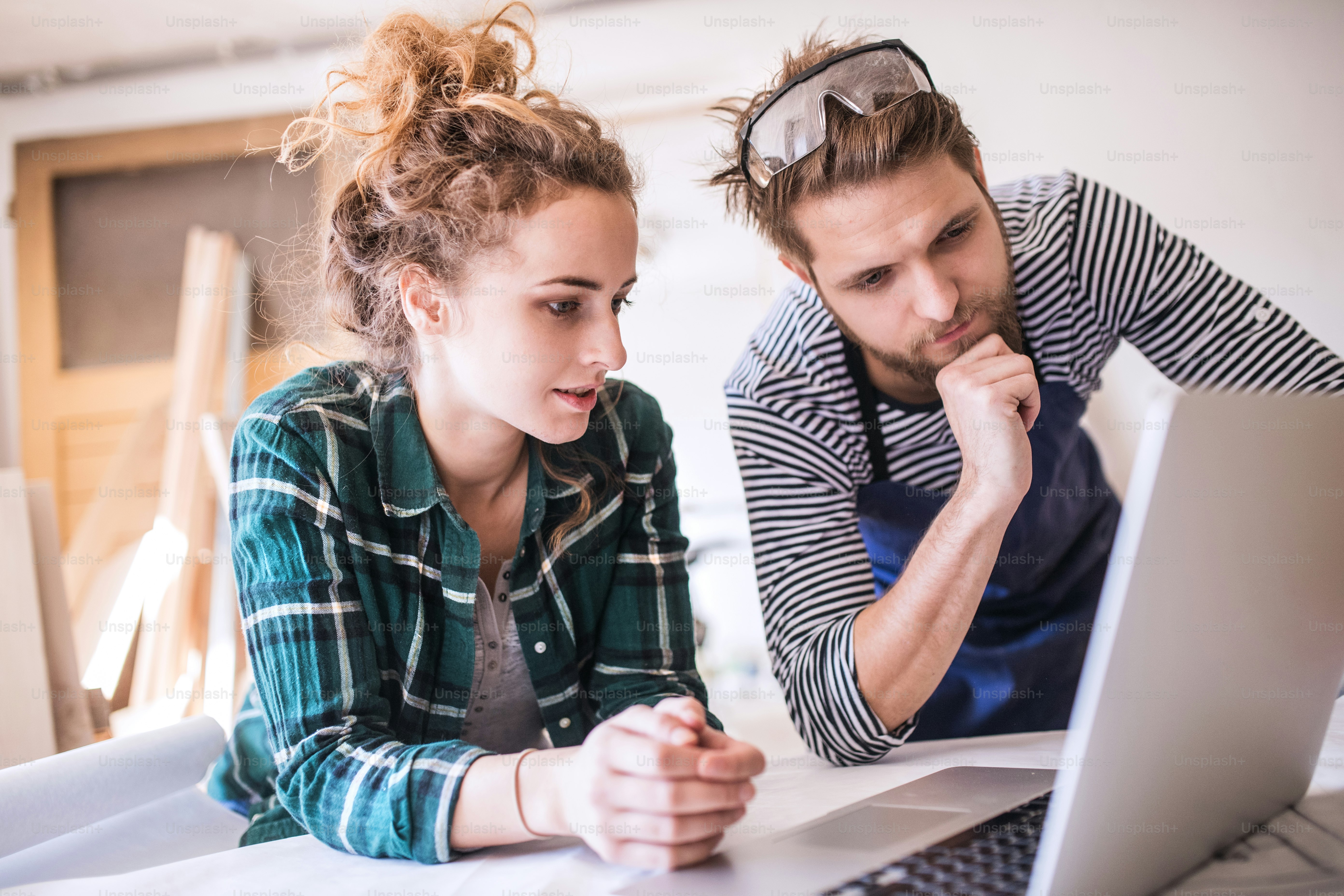 Homme et femme avec un ordinateur portable dans la salle de travail du menuisier. Jeune couple travaillant ensemble.