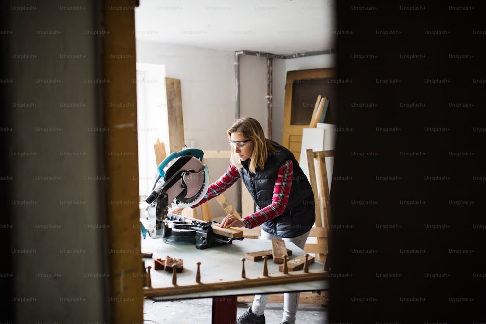 Young woman worker in workroom. Female carpenter using miter saw.