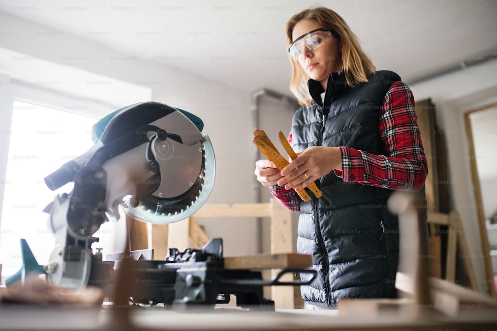 Young woman worker in workroom. Female carpenter using miter saw.