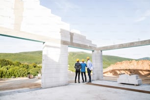 Architect, civil engineer and worker looking at plans and blueprints, discussing issues at the construction site. Rear view.