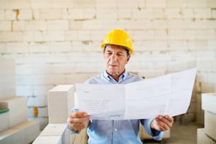 Senior architect or civil engineer at the construction site with blueprints, controlling issues at the construction site.