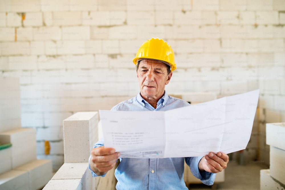 Senior architect or civil engineer at the construction site with blueprints, controlling issues at the construction site.
