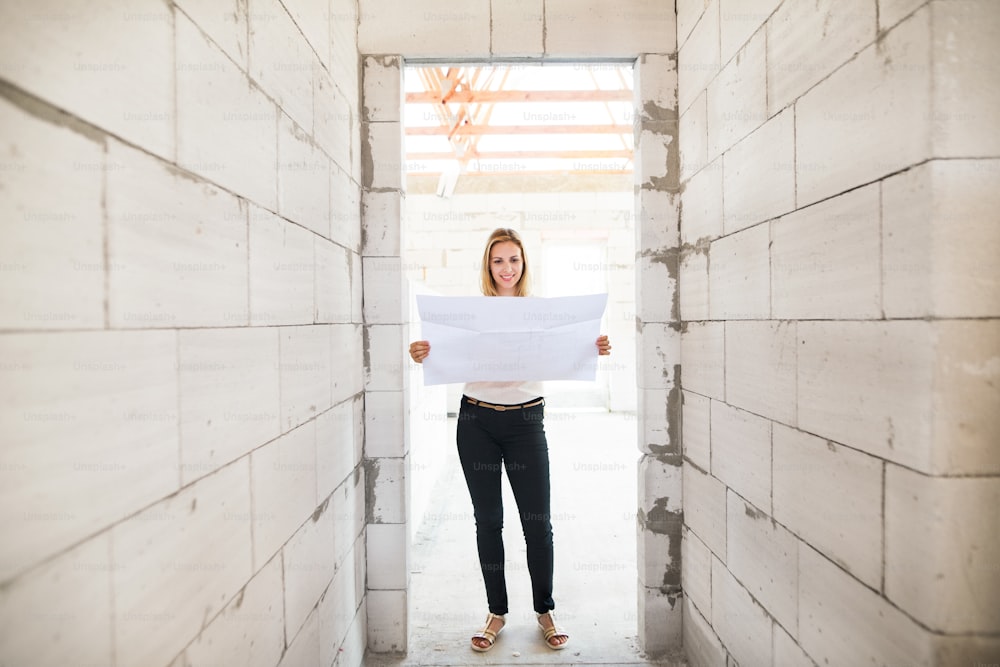 Young woman at the construction site. Woman looking at plans of the new house, discussing issues at the construction site.