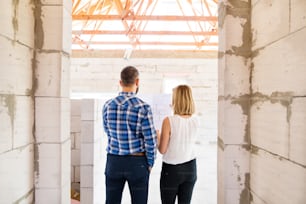 Young couple at the construction site. A man and woman looking at plans of the new house, discussing issues at the construction site. Rear view.