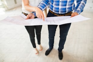 Unrecognizable young couple at the construction site. A man and woman looking at plans of the new house, discussing issues at the construction site.